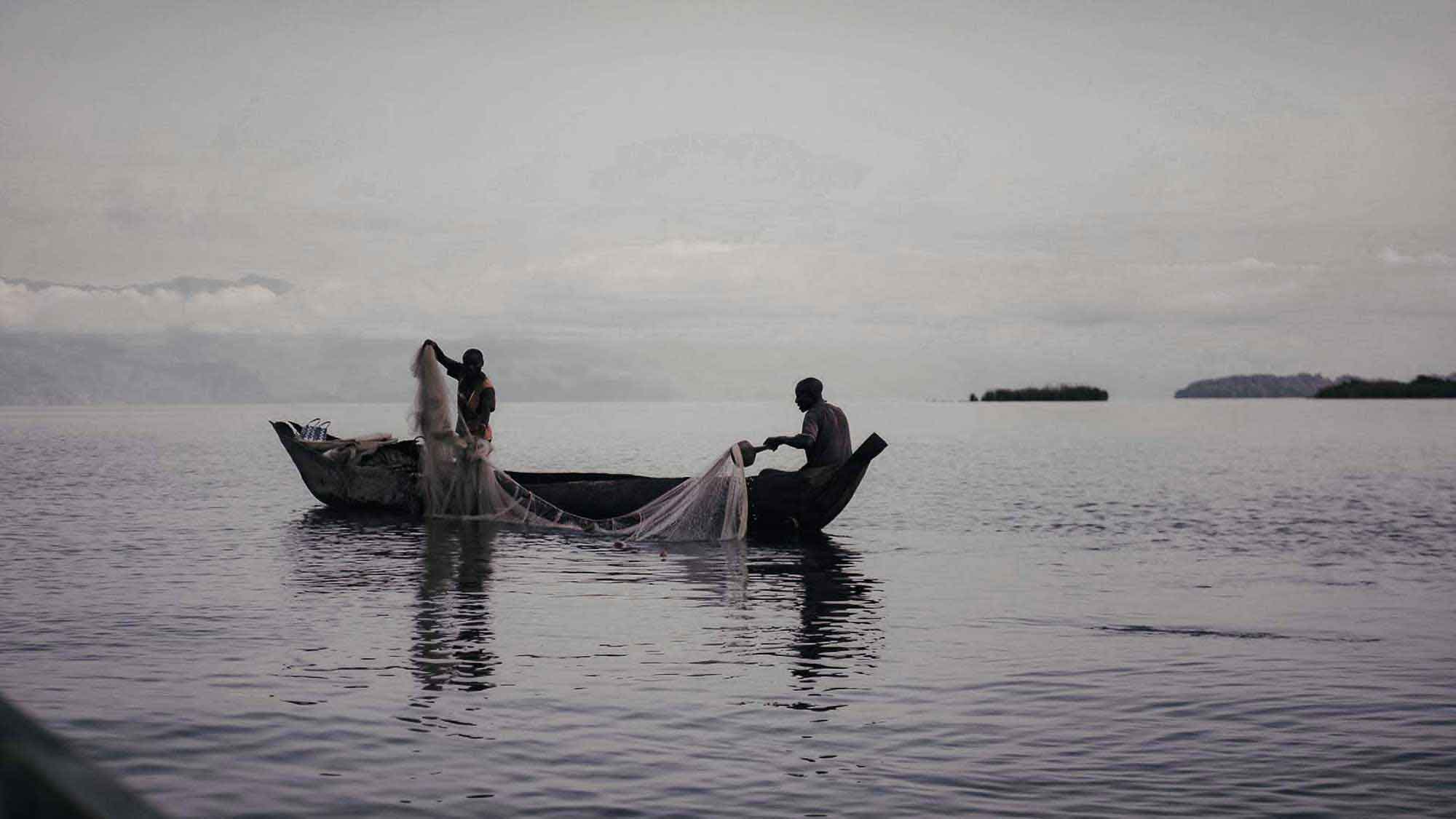 piroguiers sur le lac kivu à la tombée de la nuit lancant leurs filets.